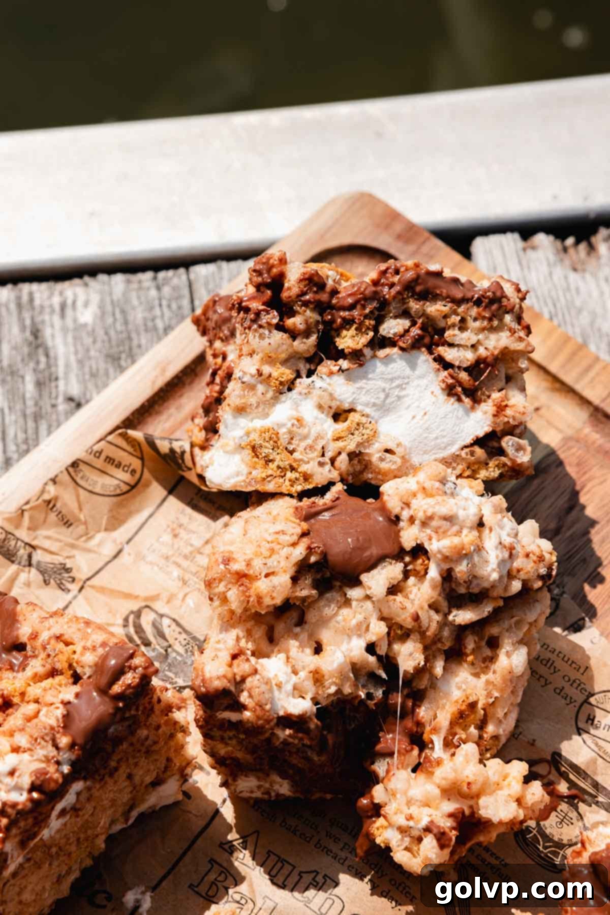 Close-up of golden S'mores Rice Krispies Treats with visible chunks of toasted marshmallow, graham cracker, and melted chocolate, showcasing their gooey texture.