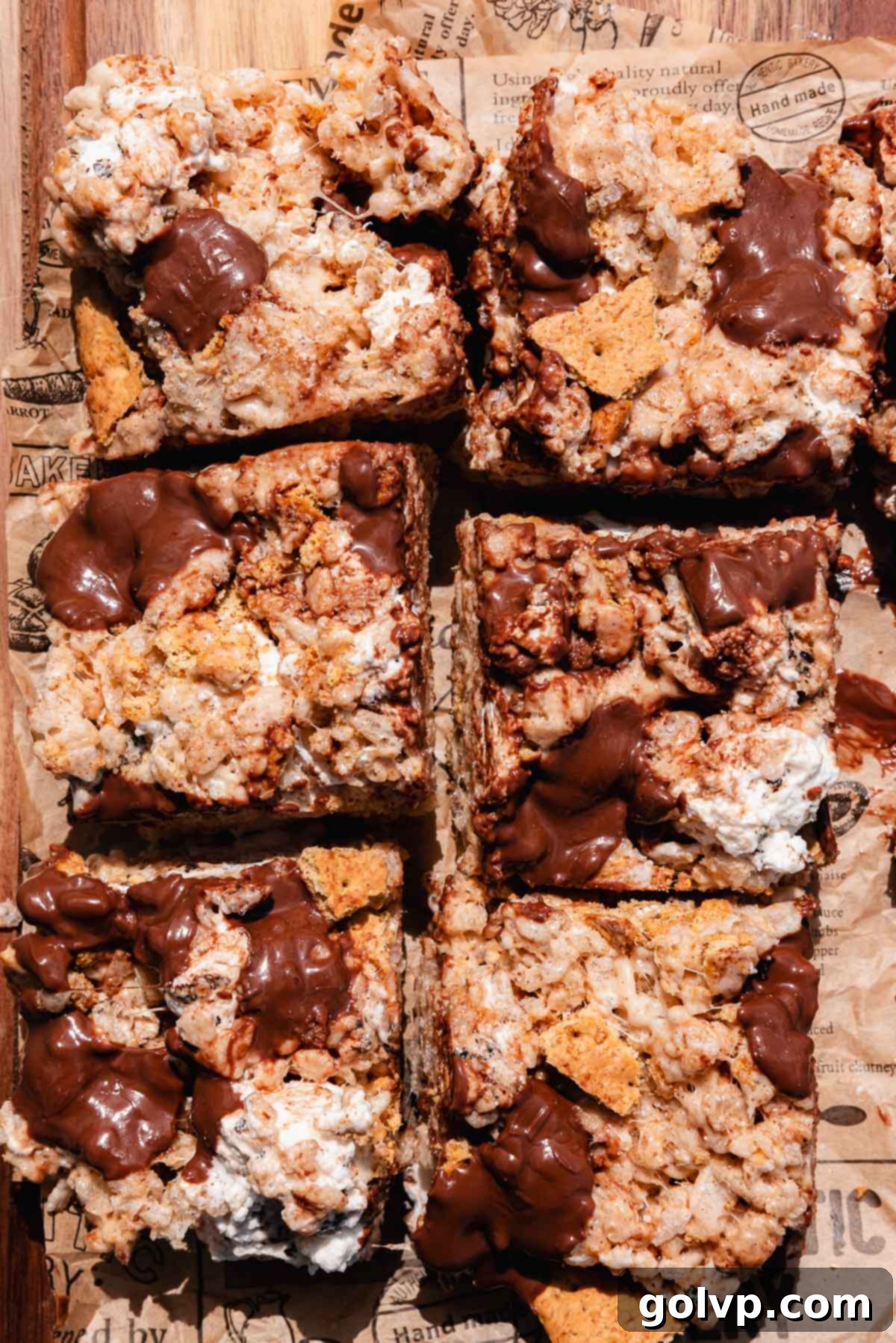 Freshly cut squares of S'mores Rice Krispies Treats arranged on parchment paper, adorned with melted chocolate pieces on top.