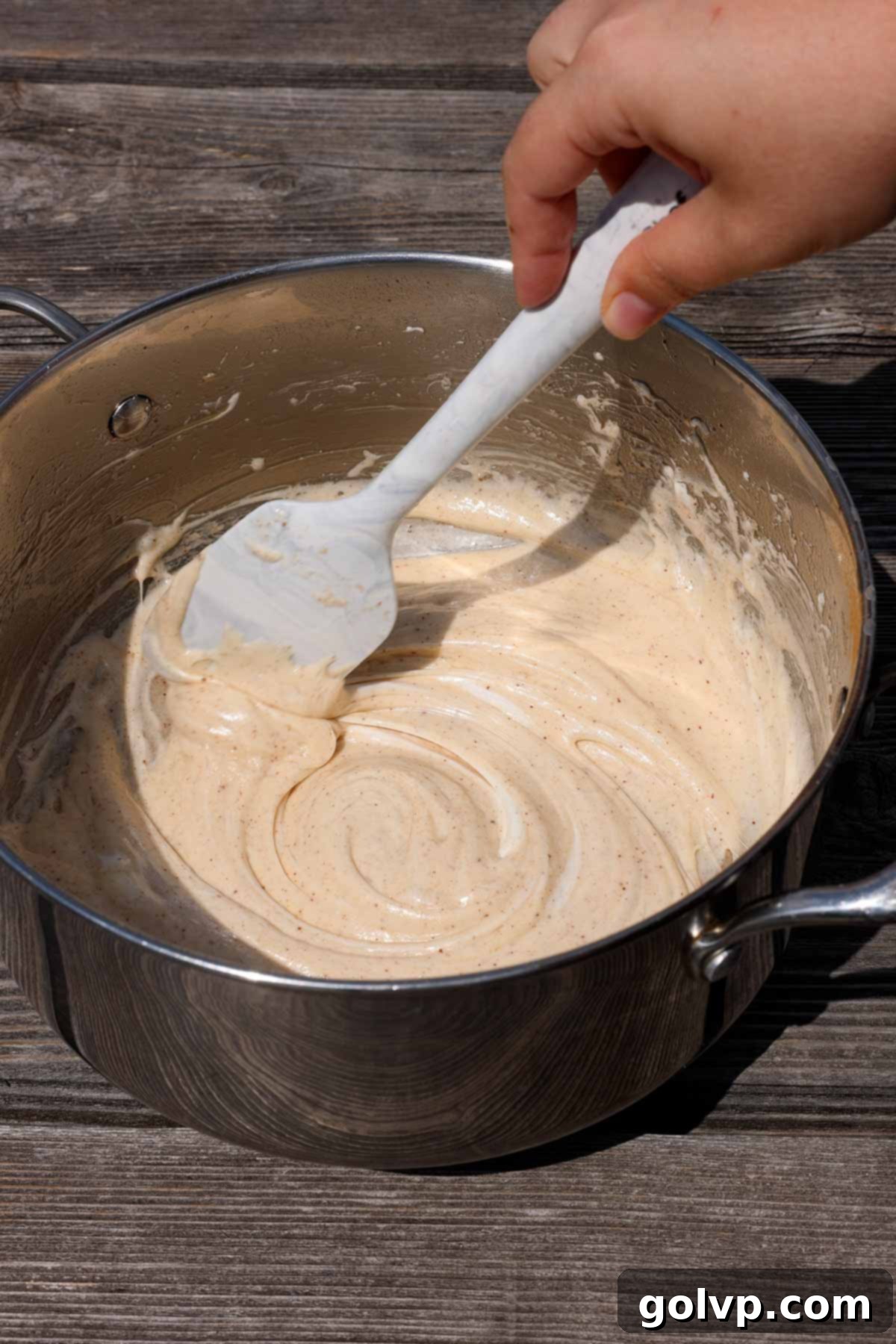 Melted marshmallows and brown butter being stirred in a heavy-bottomed pot with a silicone spatula, creating a rich, golden mixture.