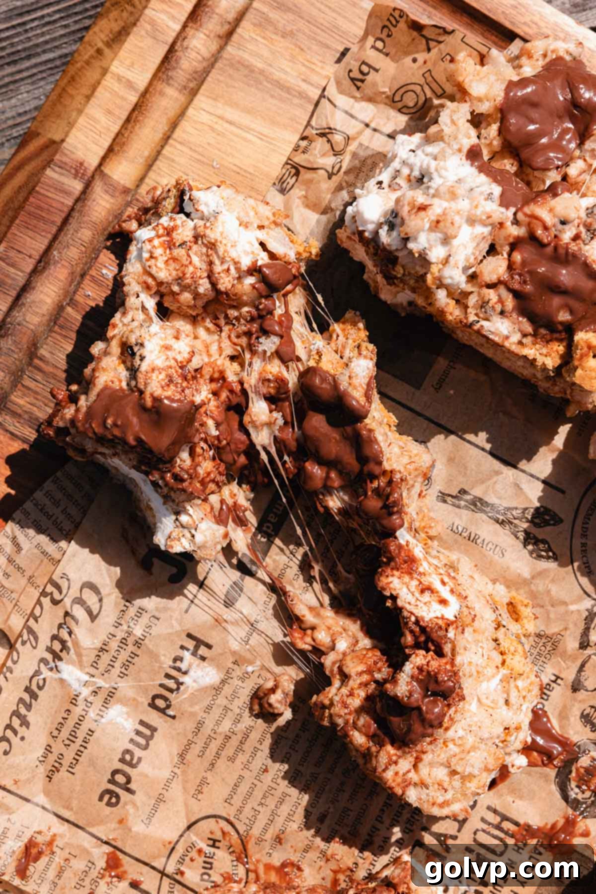 A single piece of S'mores Rice Krispies Treat held up, showing a long, stretchy, gooey marshmallow pull between the two halves.