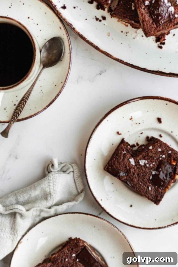 Two plates with square brownie pieces, one with a fork, beside a cup of coffee, suggesting a delightful treat.