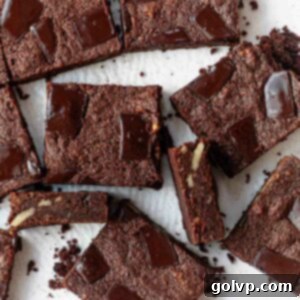 Several square brownie pieces scattered on a light baking sheet, showcasing their rich texture.