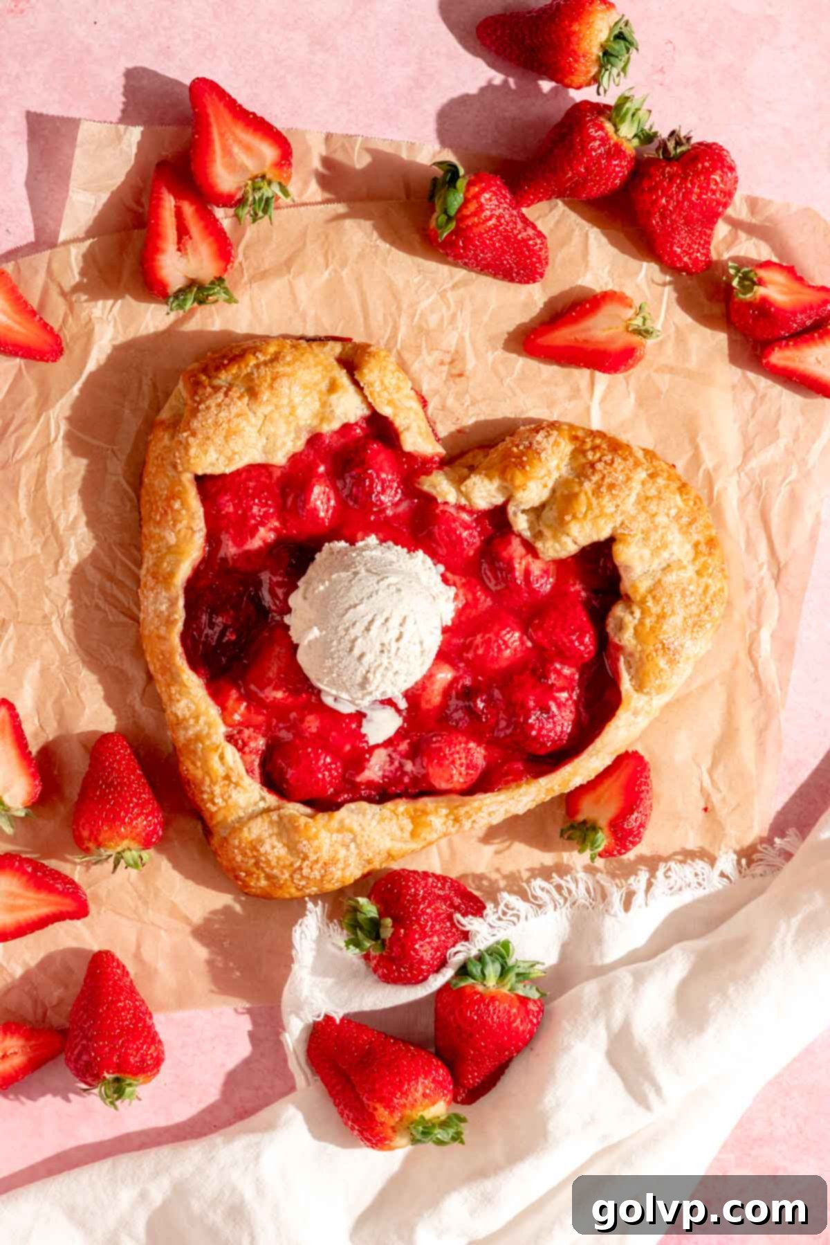 A heart-shaped strawberry galette accompanied by a scoop of melting vanilla ice cream, showcasing its rustic beauty.