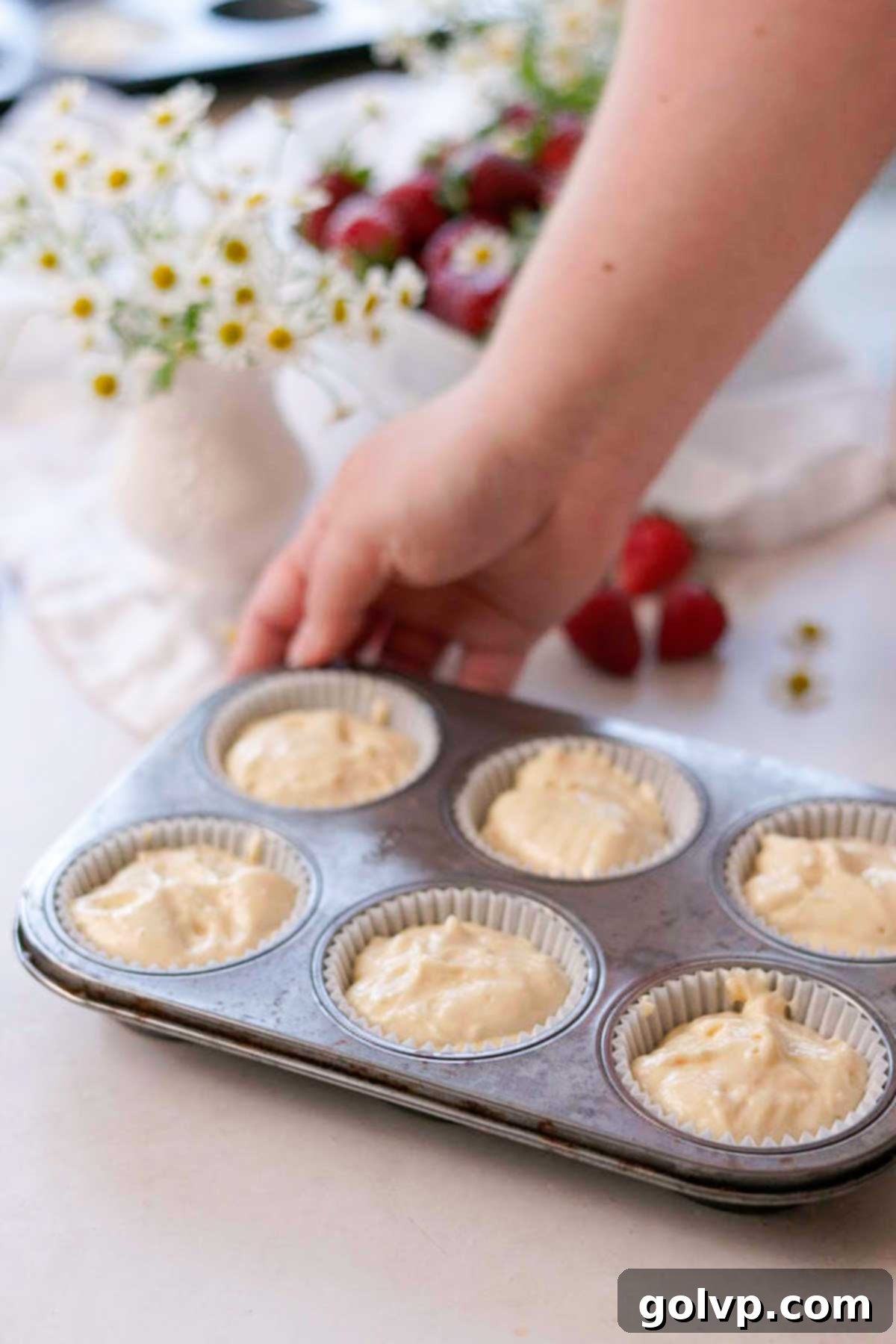 Vanilla cupcake batter evenly scooped into paper liners inside a muffin tin, ready for baking.