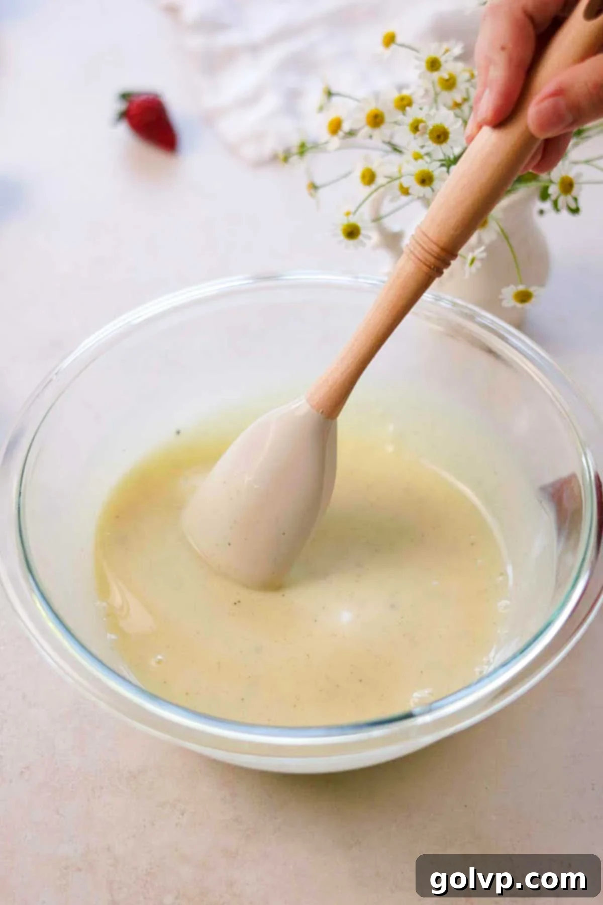 melted white chocolate ganache being mixed in a glass bowl with a spatula