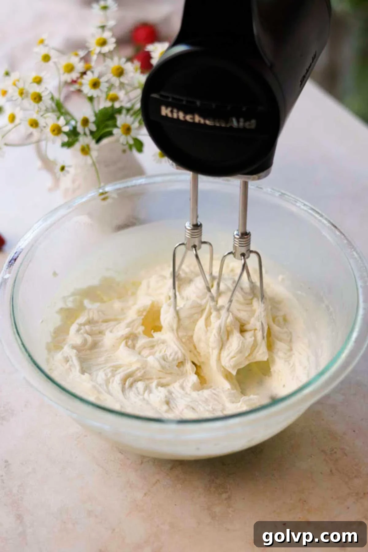 a hand held electric mixer whipping white chocolate ganache in a glass bowl