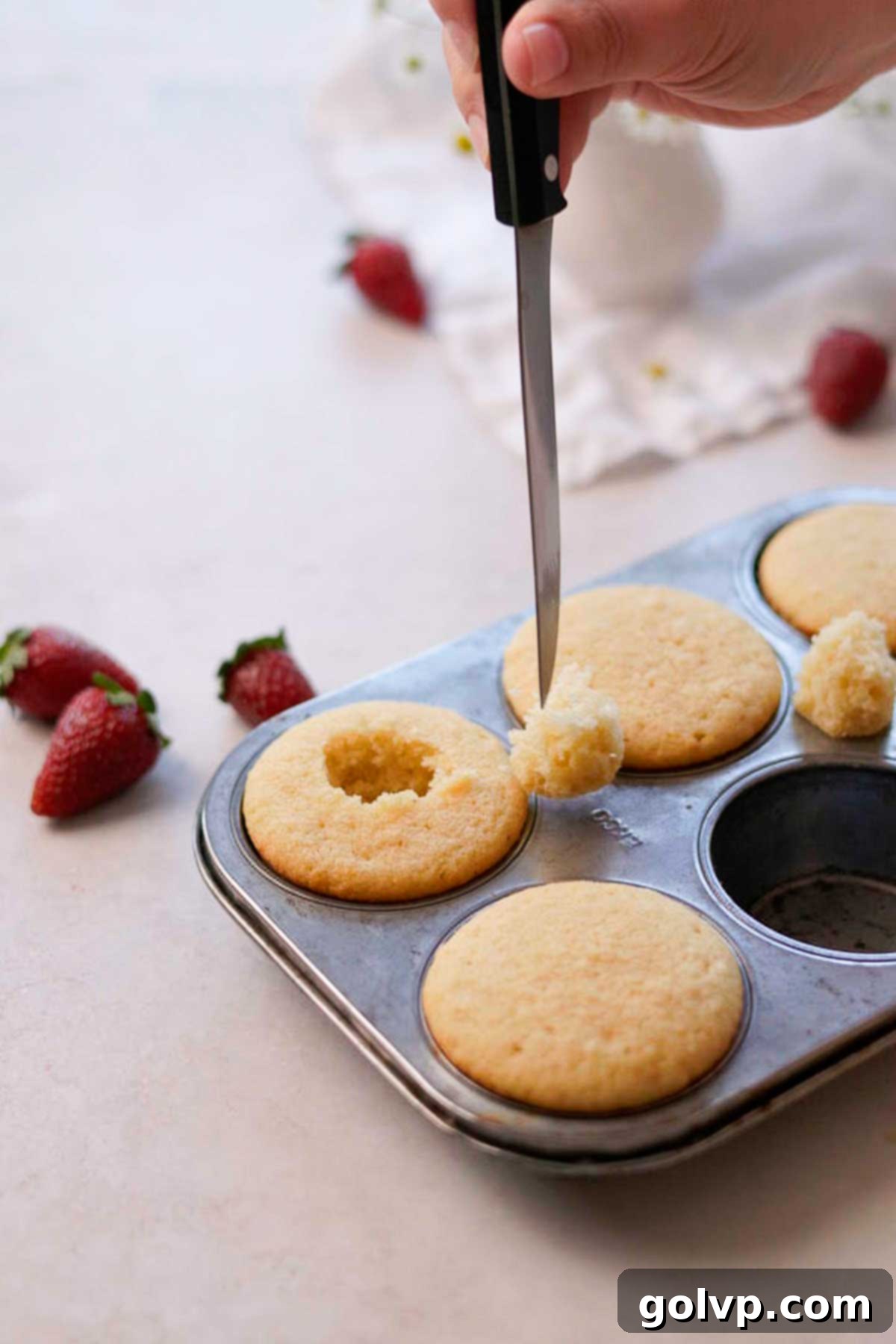 A small, sharp knife carefully cutting out the center of a baked vanilla cupcake to create a cavity for filling.