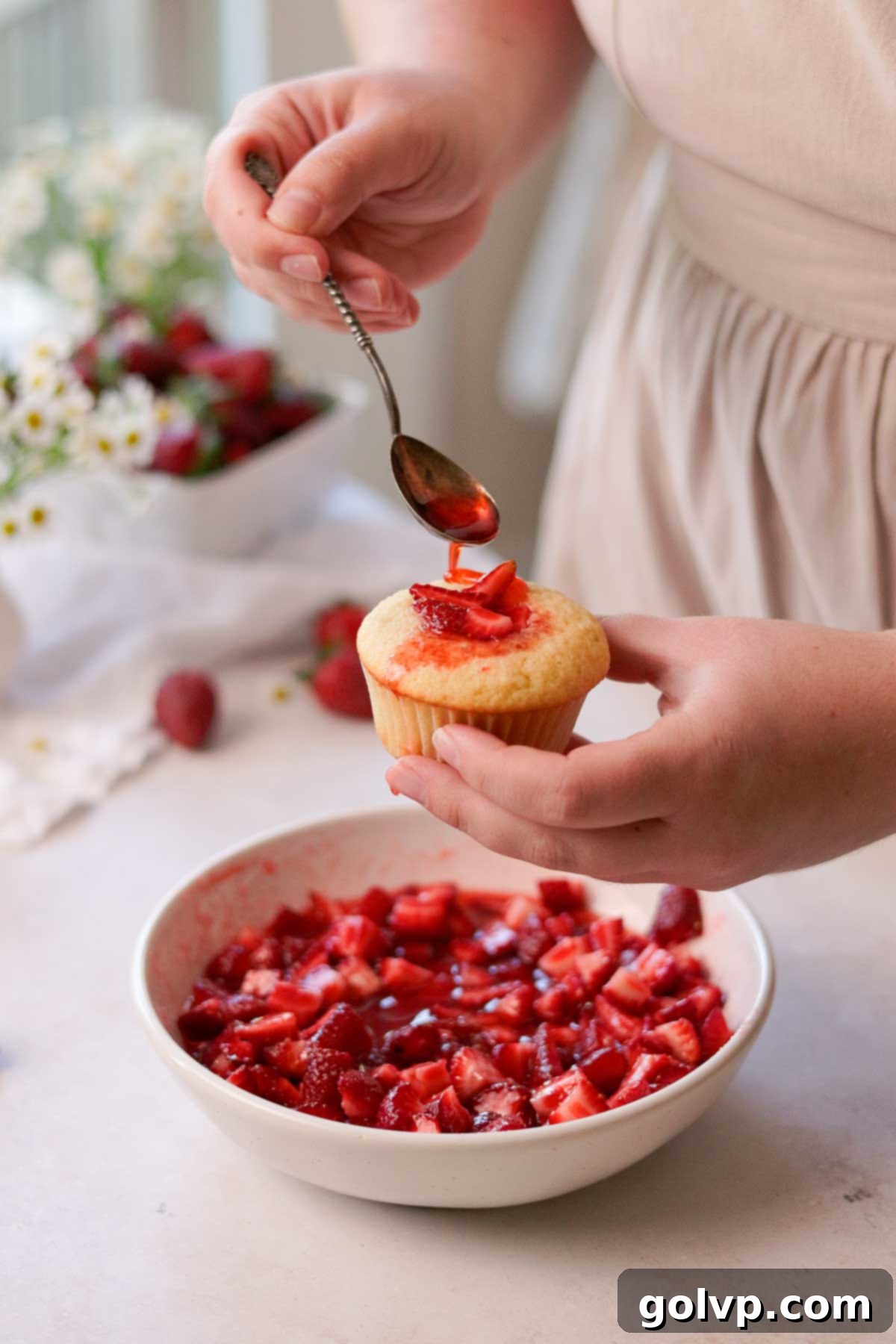 A cupcake being filled with macerated strawberry pieces, with extra syrup being drizzled over the top for added moisture and flavor.