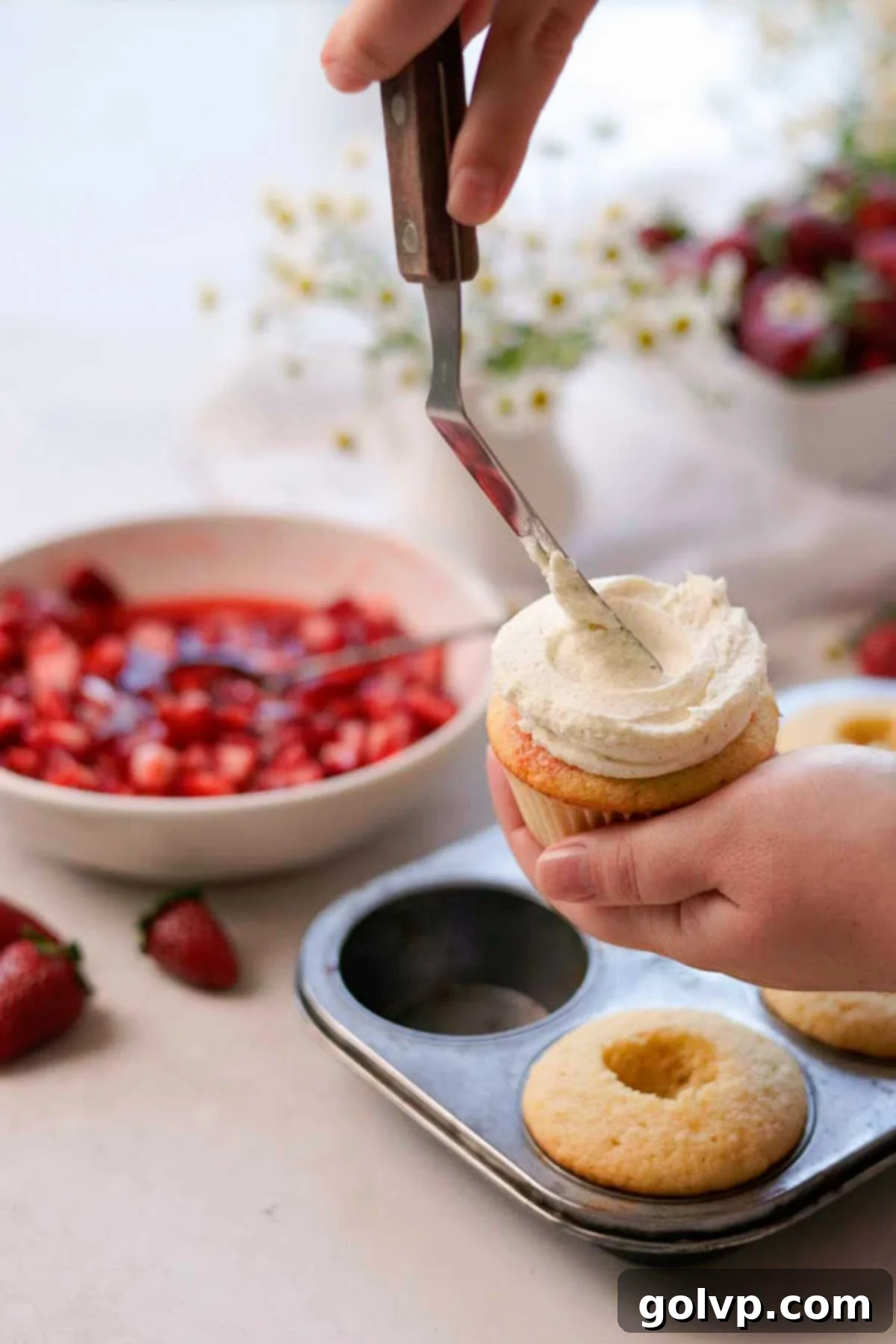 adding white chocolate mousse frosting to the cupcakes with a metal spatula