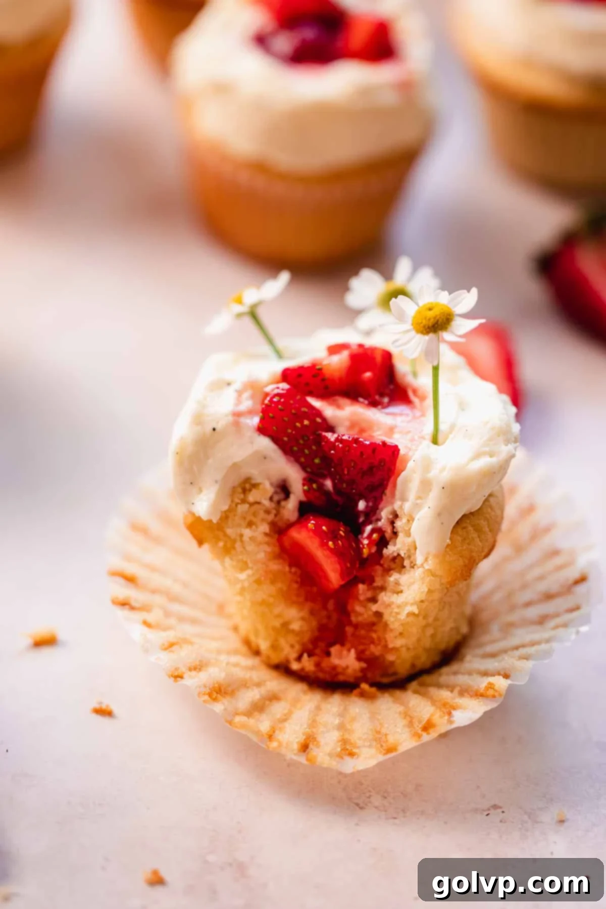 a close up shot of a bitten strawberry white chocolate cupcake with strawberries inside and flowers on top