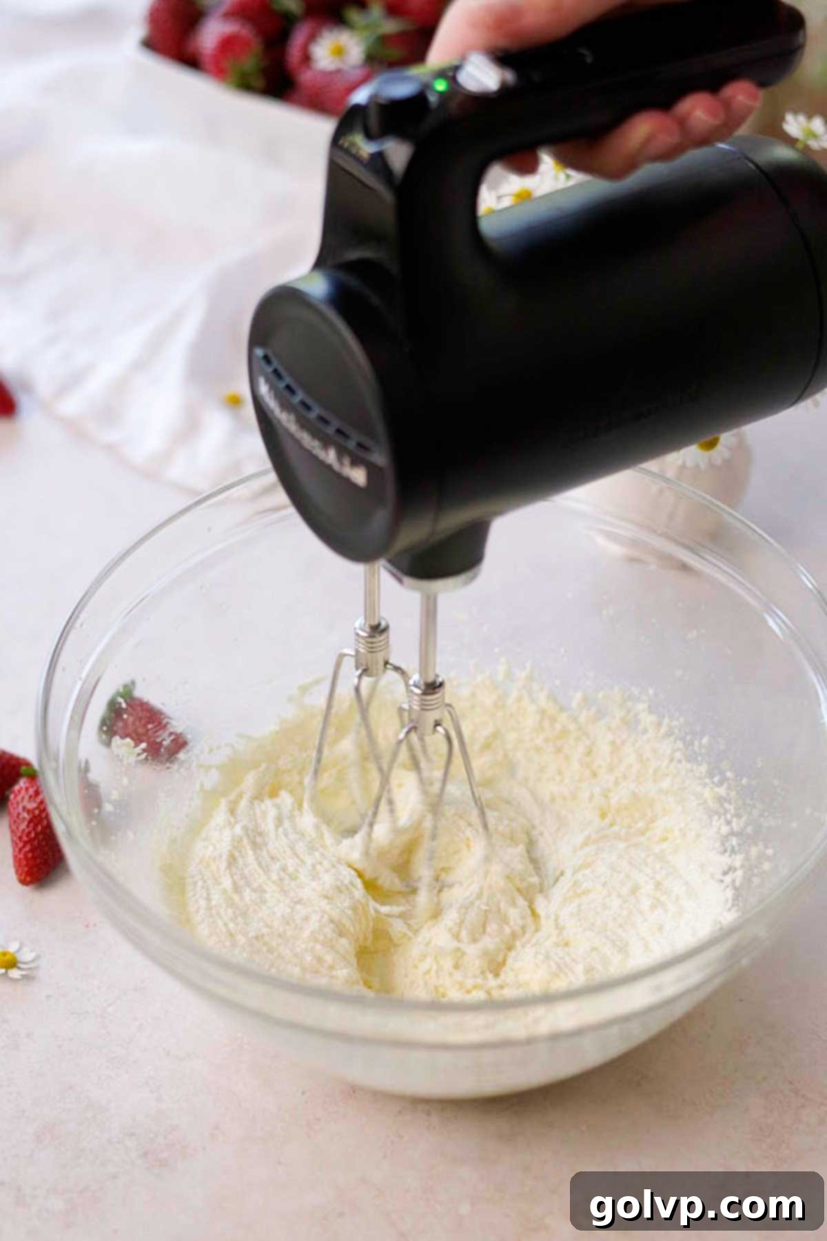 Sugar, softened butter, and olive oil being creamed together in a clear glass bowl using a hand-held electric mixer until light and fluffy.