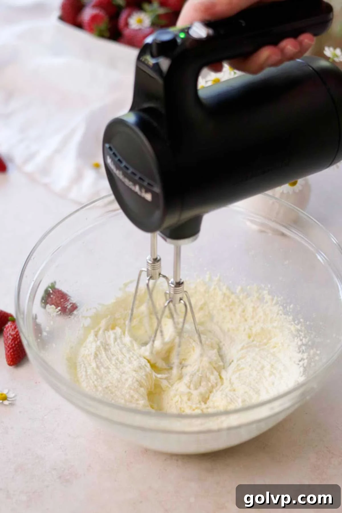sugar, butter, and oil being whipped in a glass bowl by a hand held electric mixer