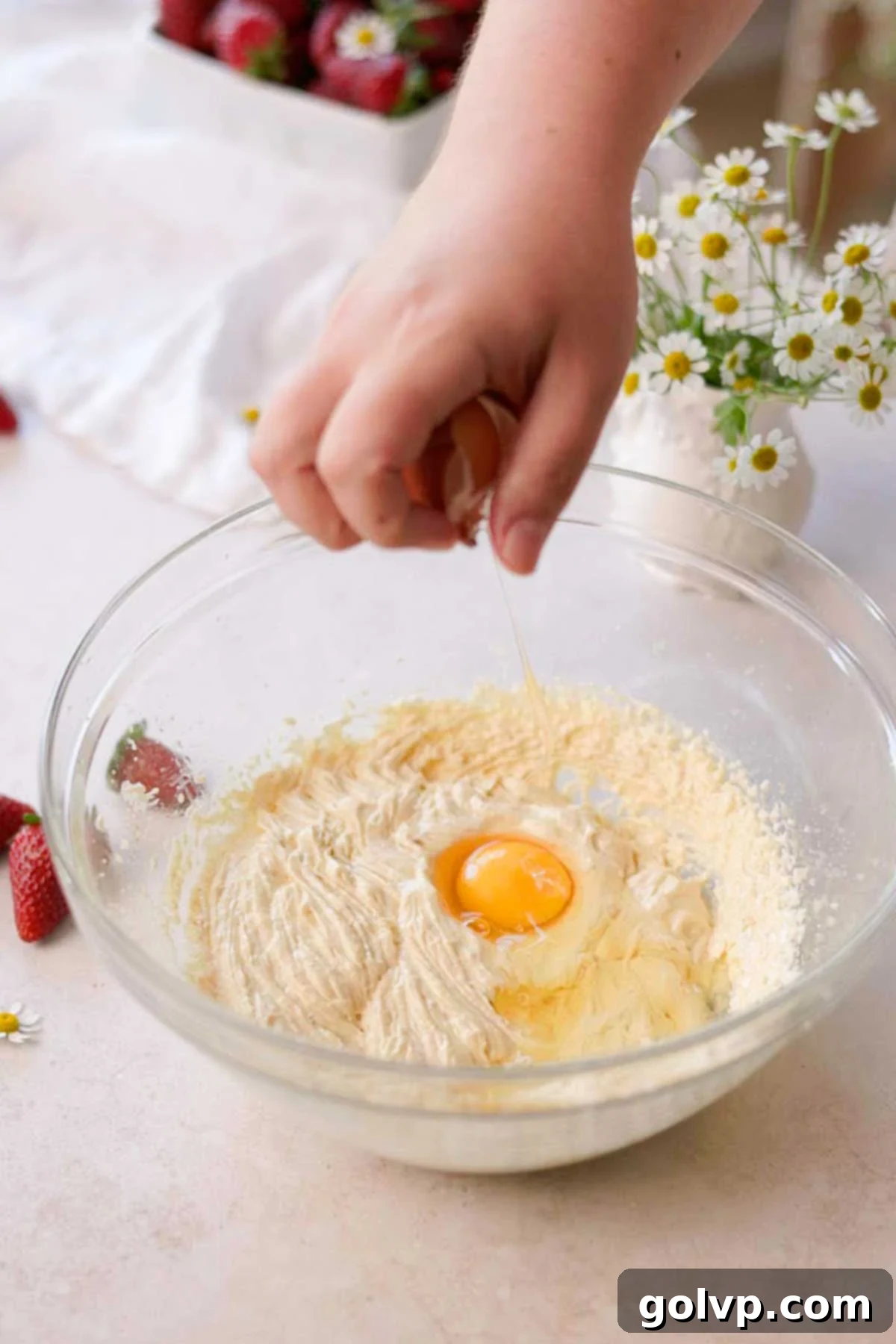 adding an egg to the cupcake batter in a glass bowl