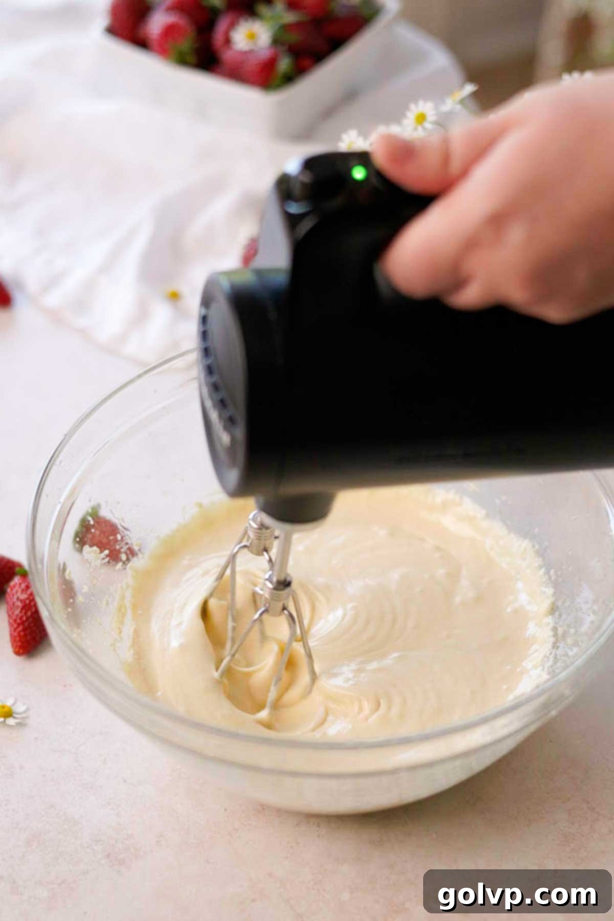Liquid wet ingredients for vanilla cupcakes, including buttermilk and vanilla, being mixed vigorously with an electric mixer in a glass bowl.