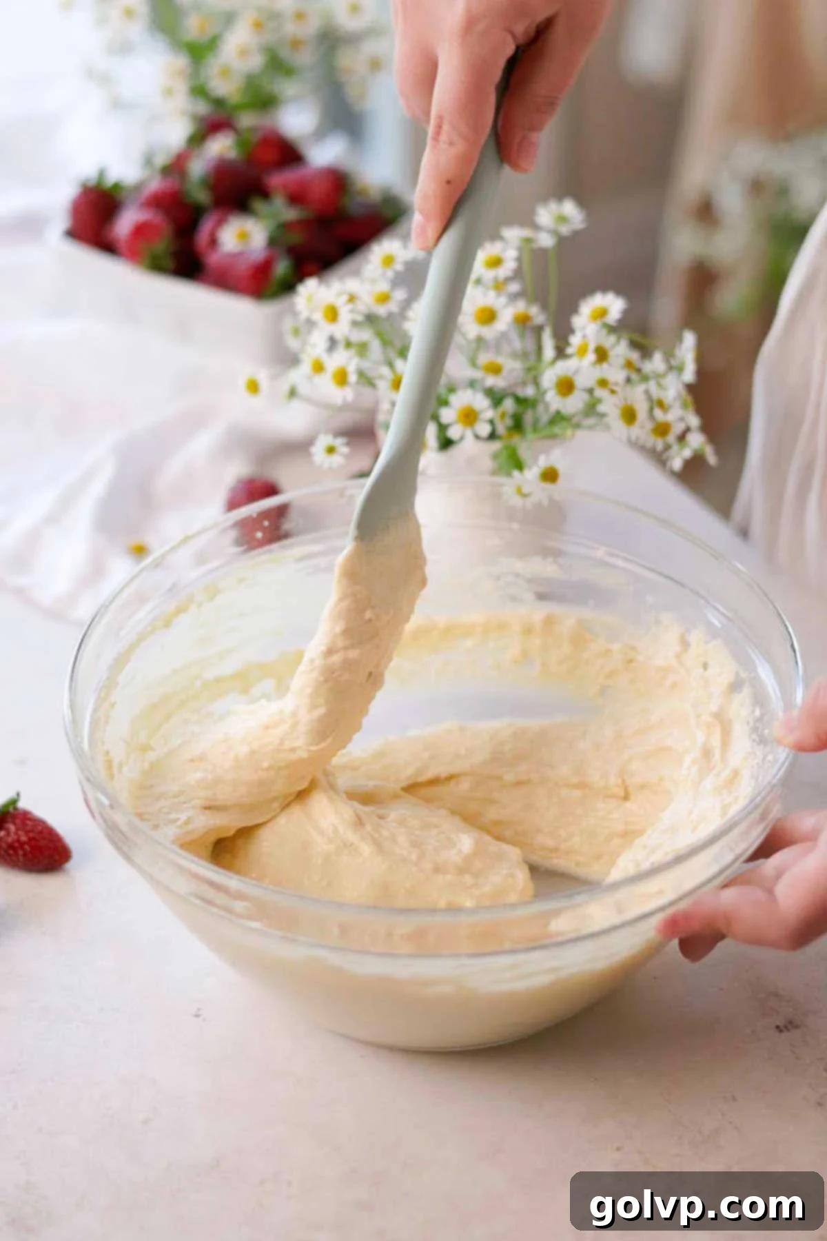 folding vanilla cupcake batter with a spatula in a glass bowl