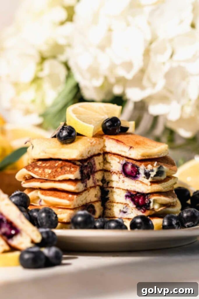 Stack of fluffy blueberry lemon ricotta pancakes with a peek inside, garnished with lemon slices and fresh blueberries, ready to be served for breakfast or brunch.