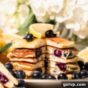 stack of blueberry lemon pancakes with peak inside. Topped with lemon slices and fresh blueberries