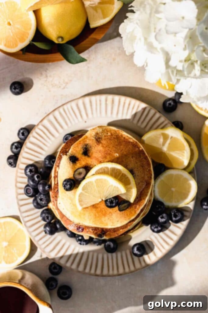 A stack of golden brown blueberry lemon ricotta pancakes on a plate, garnished with fresh lemon slices and delicate white flowers, perfect for a gourmet breakfast.