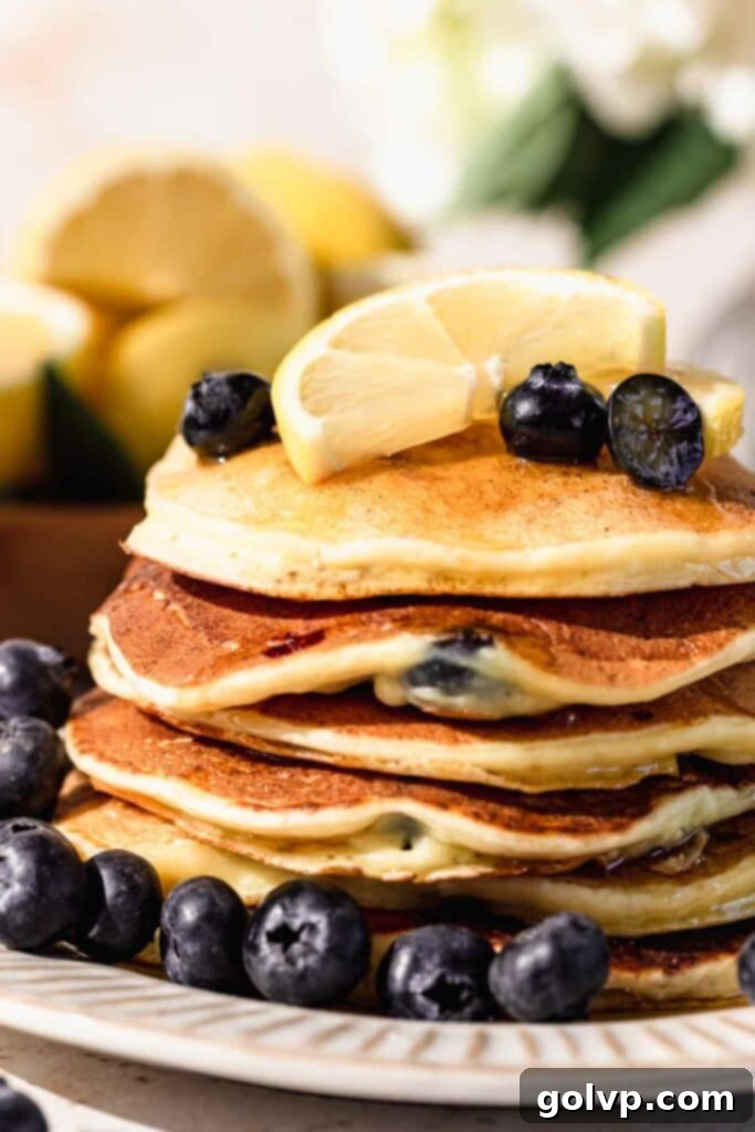 Close-up shot of a stack of golden blueberry lemon ricotta pancakes, showcasing their fluffy texture and juicy blueberry distribution, a perfect breakfast treat.