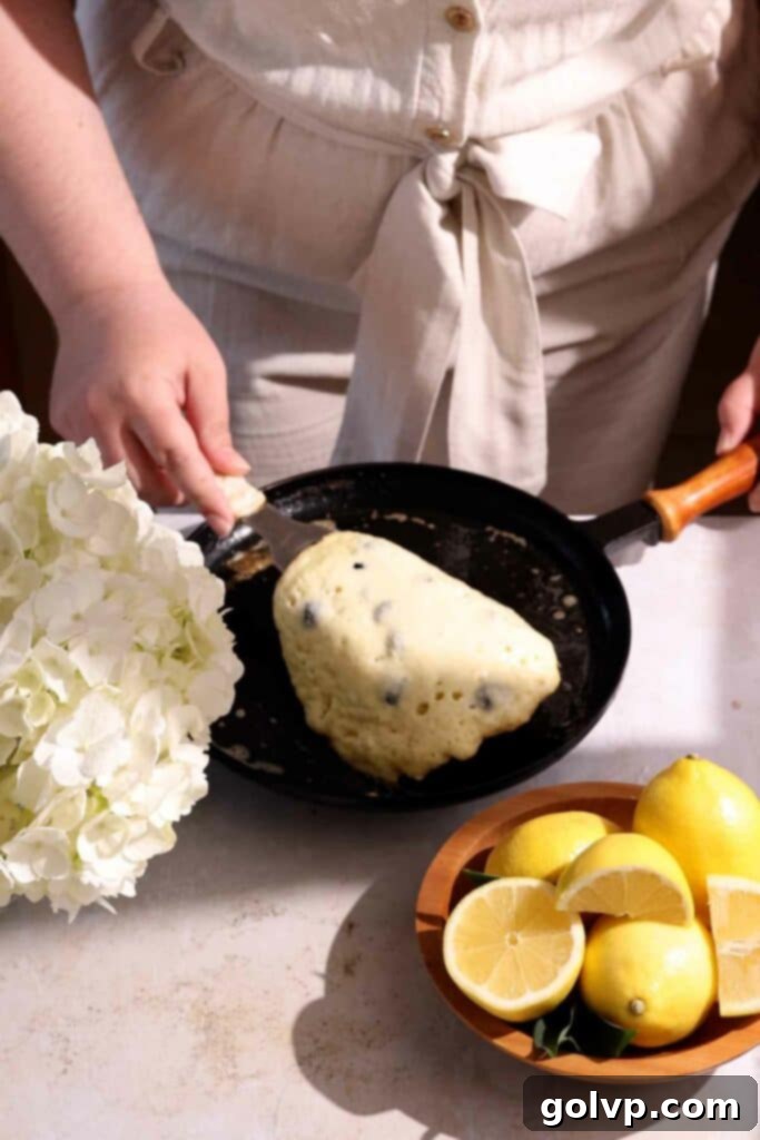 Flipping a golden-brown blueberry lemon ricotta pancake in a hot skillet, showing the cooking process for a perfect breakfast.