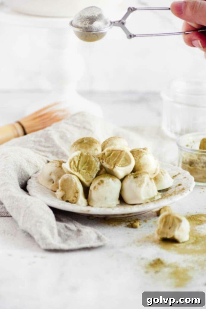 Delicately sprinkling bright green matcha powder over freshly dipped white chocolate truffles arranged on parchment paper.
