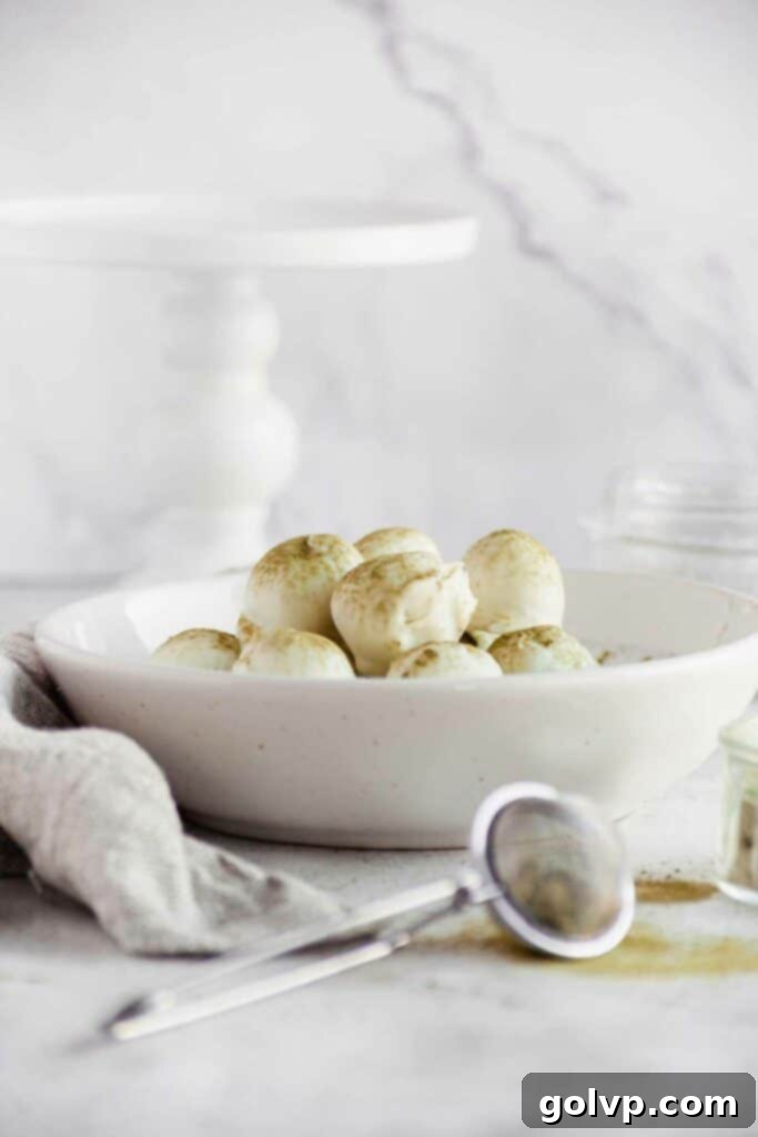 A rustic wooden bowl brimming with freshly made matcha white chocolate truffles, dusted with green tea powder.