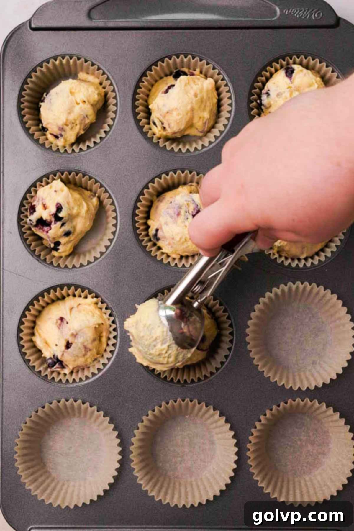 Blueberry cupcake batter being scooped into cupcake liners in a baking tray.