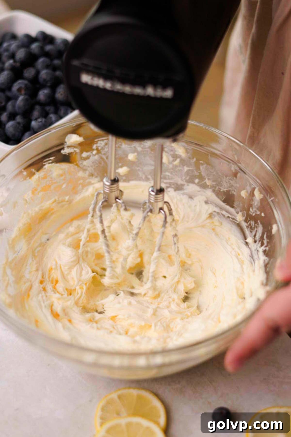 Softened butter being beaten with an electric mixer in a large glass bowl.