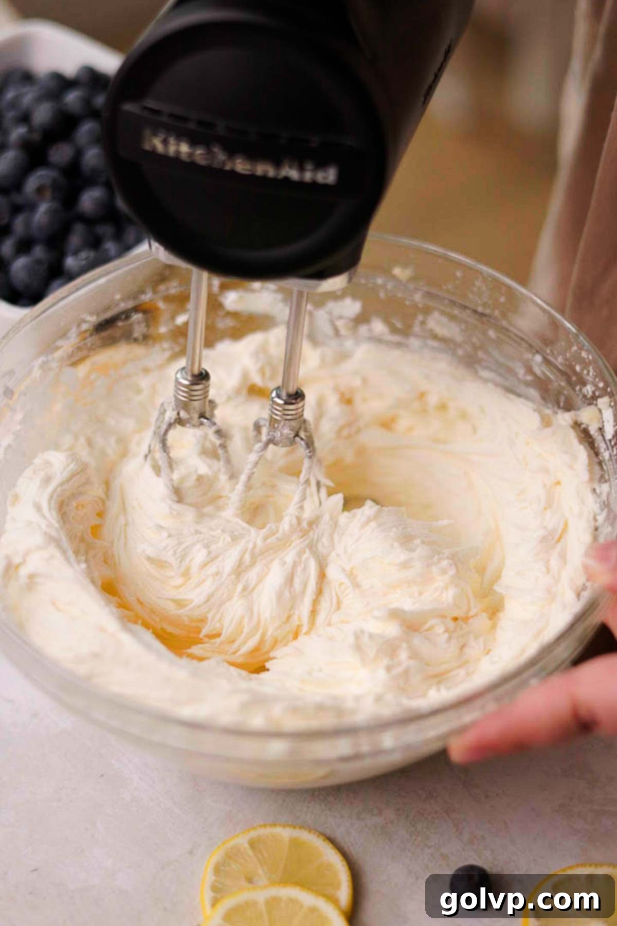 Cream cheese being beaten into the frosting base with an electric mixer.