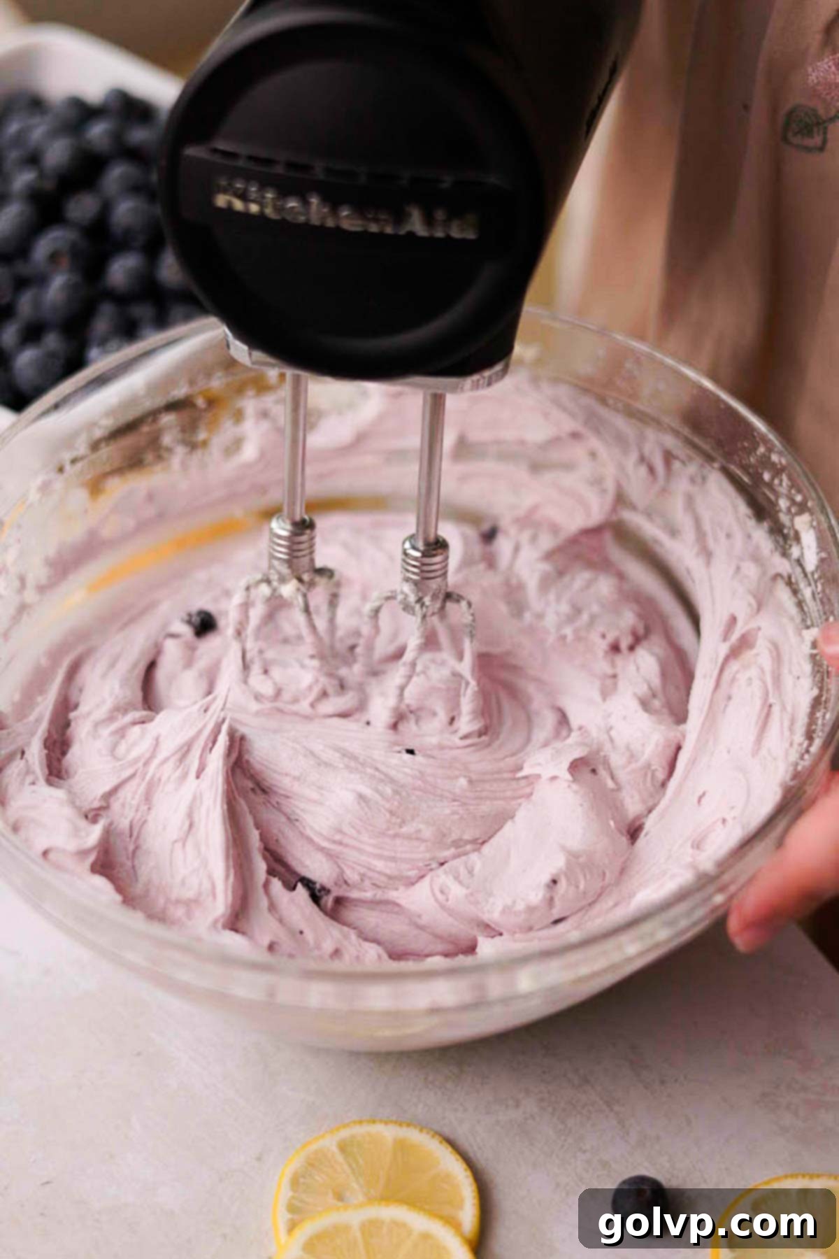 Blueberry cream cheese frosting being beaten with an electric mixer, showing its pastel purple color.