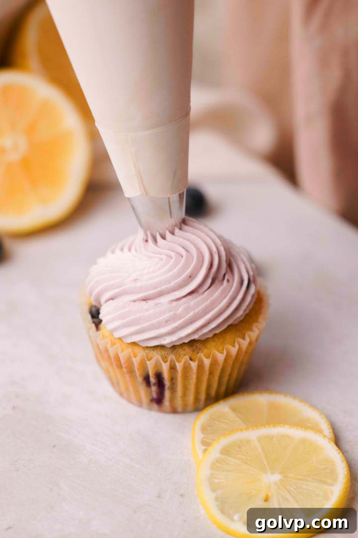 Blueberry cream cheese frosting being piped decoratively onto a filled blueberry cupcake.