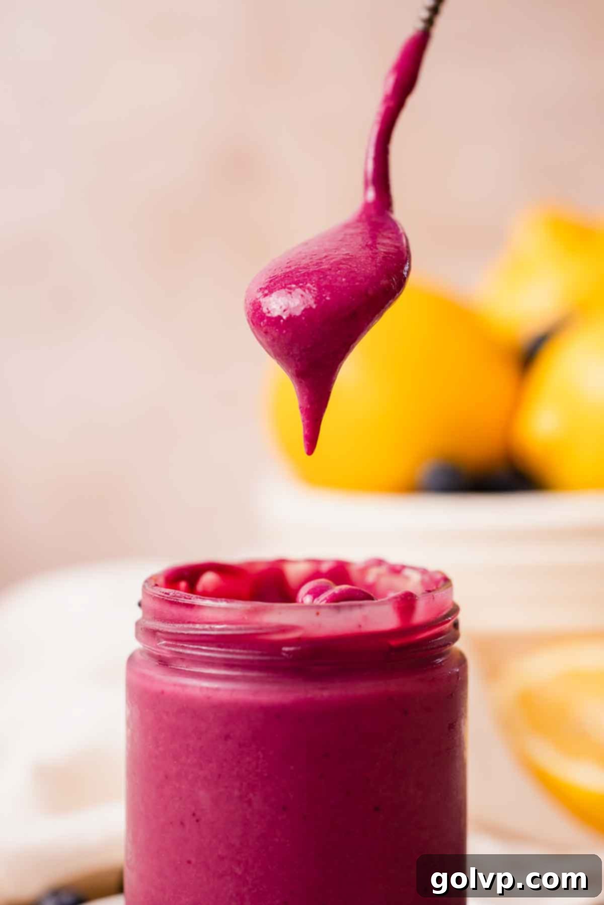 A spoonful of bright purple blueberry curd dripping from a spoon over a jar, showing its thick texture.