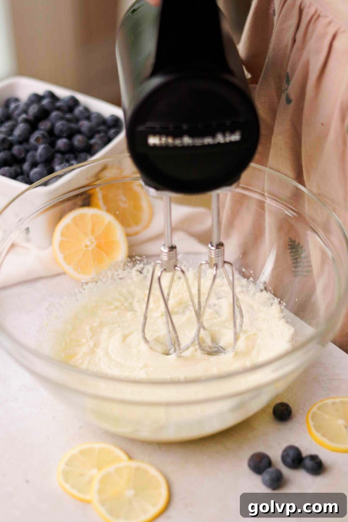 Softened butter, oil, and granulated sugar being beaten together in a large glass bowl with an electric mixer.