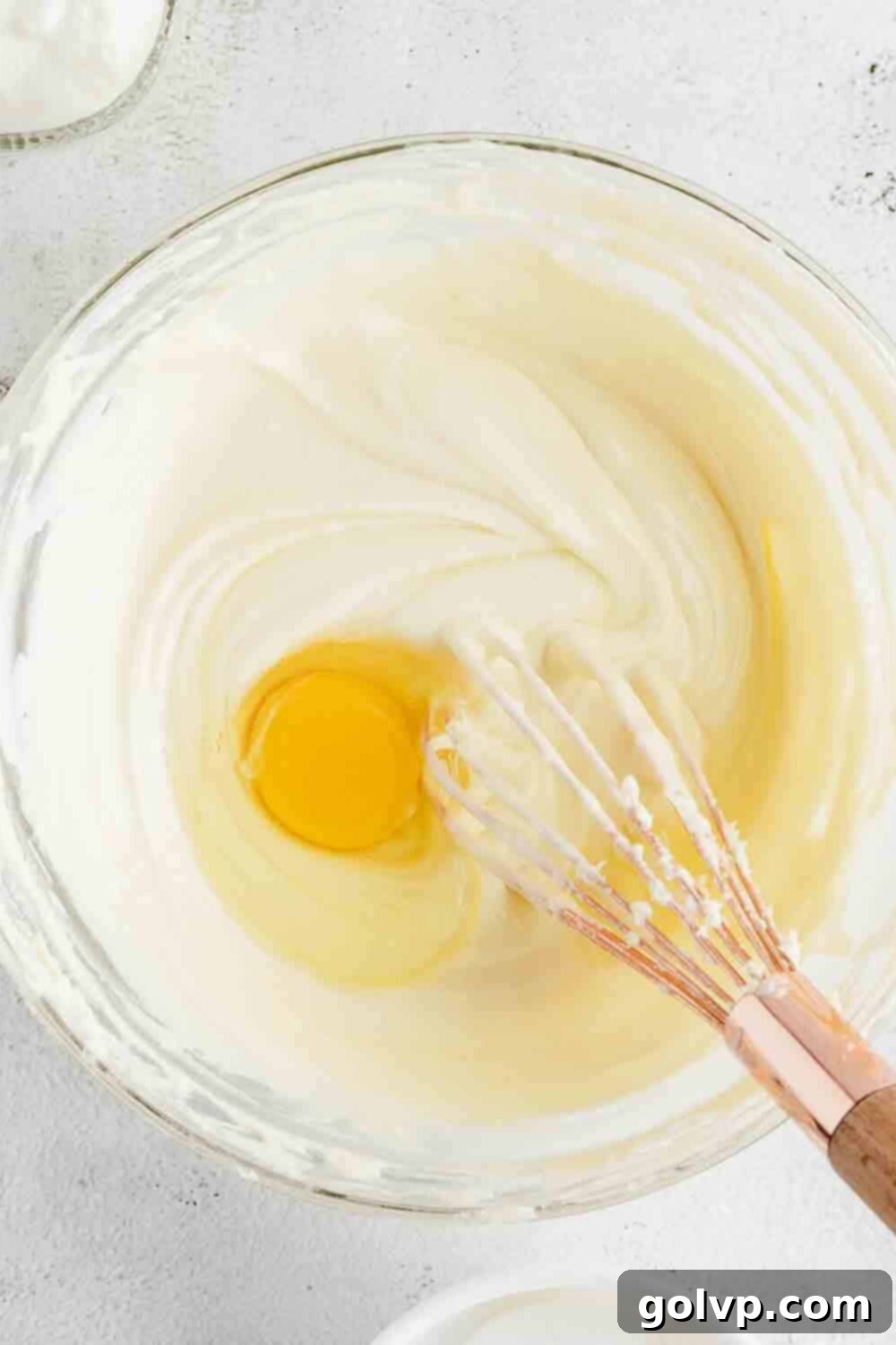 Adding egg into the beaten cream cheese and sugar mixture for the cheesecake batter.