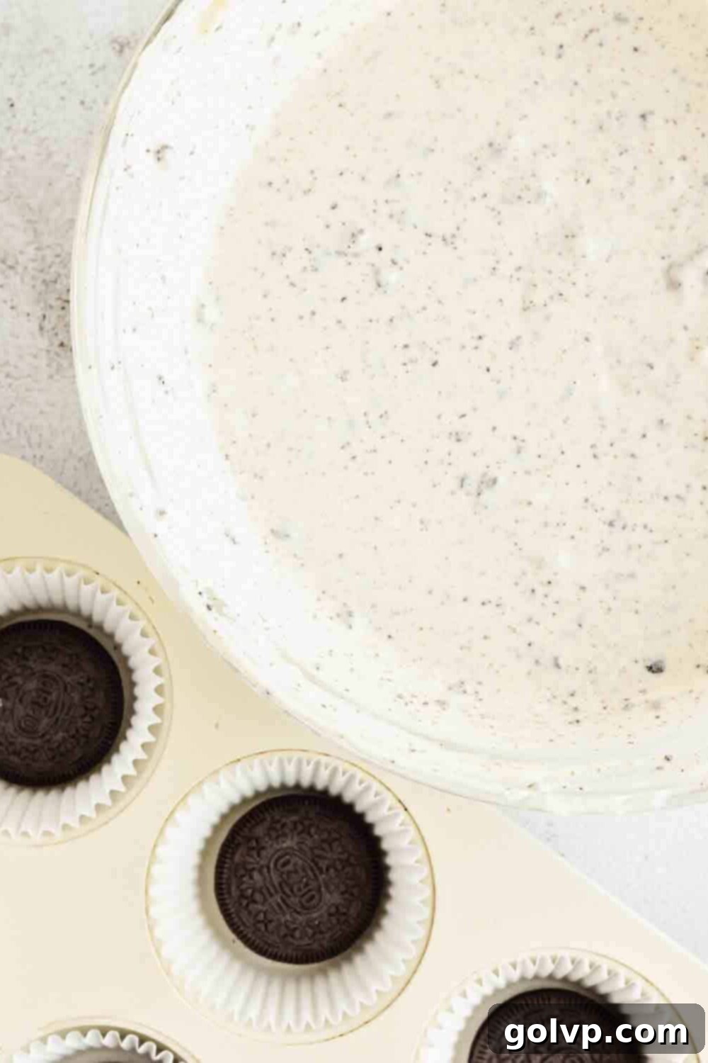 Pouring cheesecake batter onto the whole Oreo cookie base in a muffin tin.