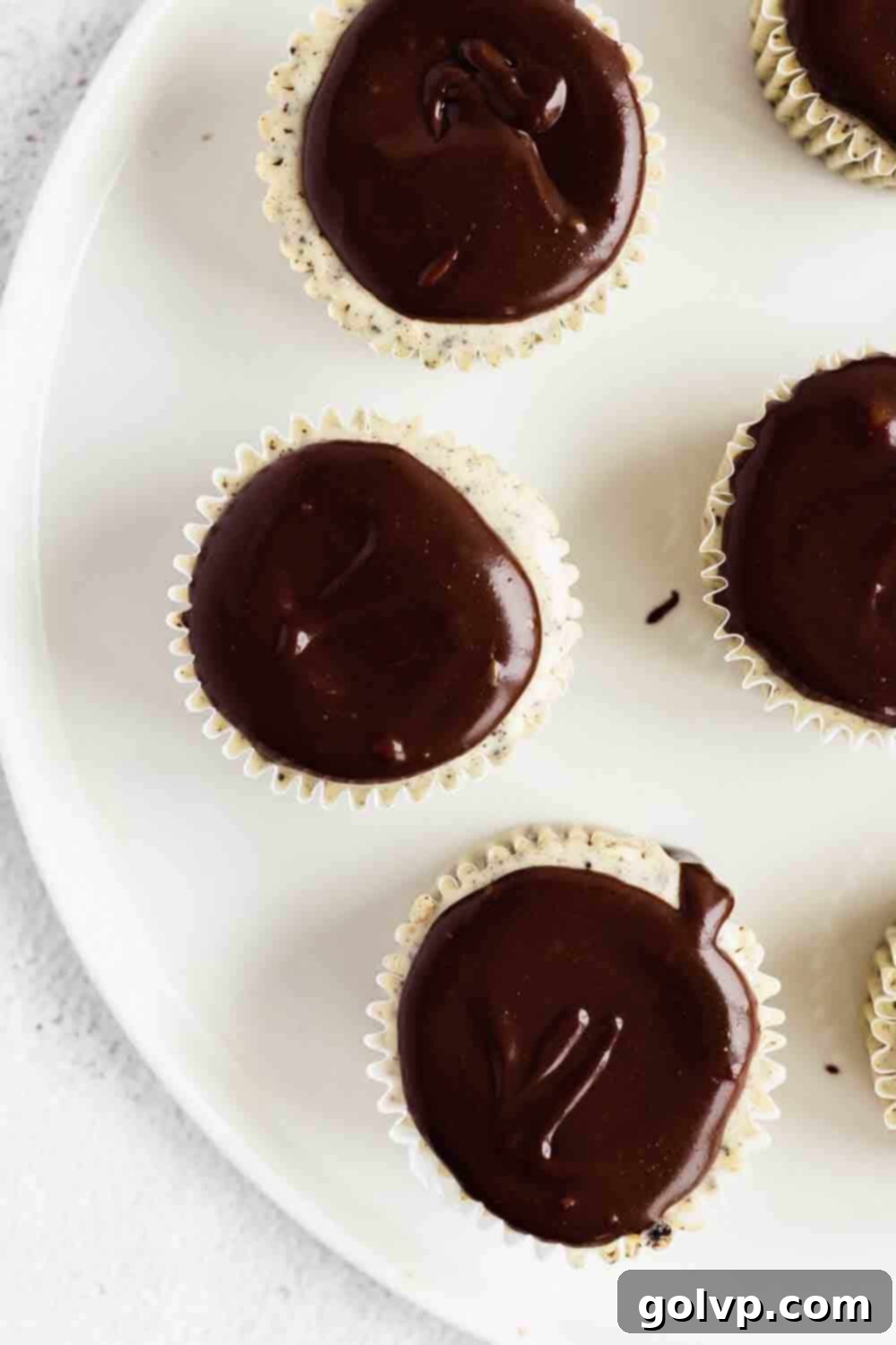 Adding a layer of chocolate fudge on top of the chilled mini cheesecakes.