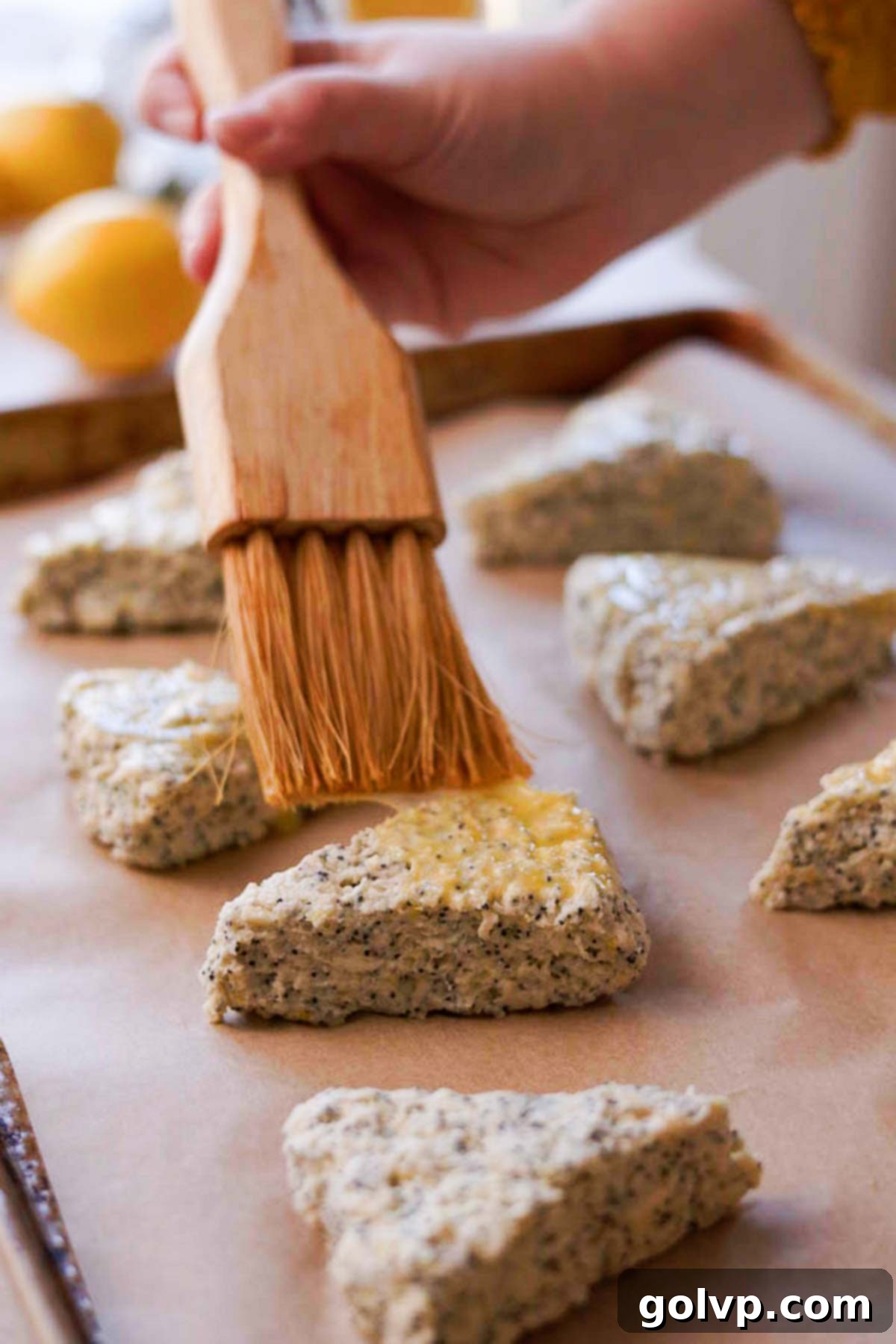 Brushing the tops of raw scone dough with egg wash using a pastry brush, avoiding the sides