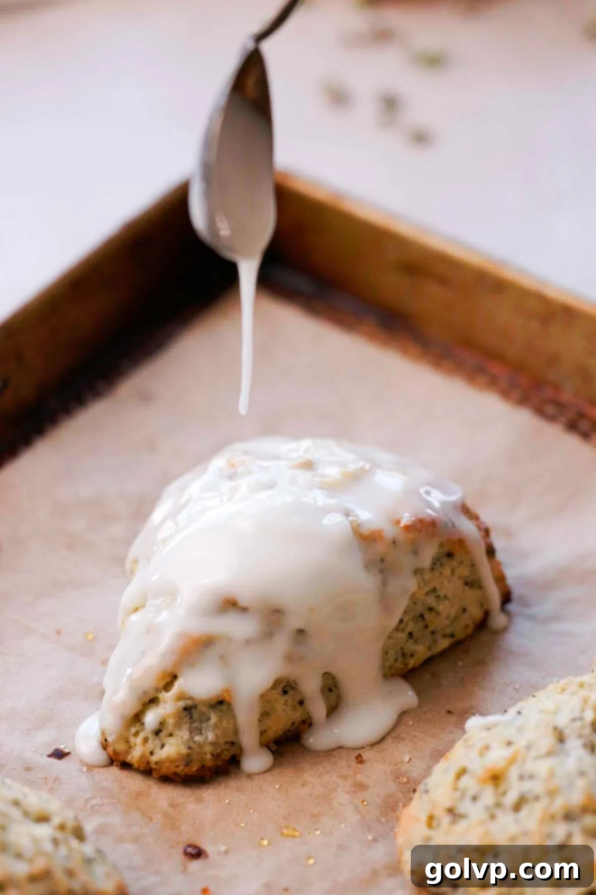 Drizzling tangy lemon glaze over freshly baked lemon poppy seed scones on a baking sheet