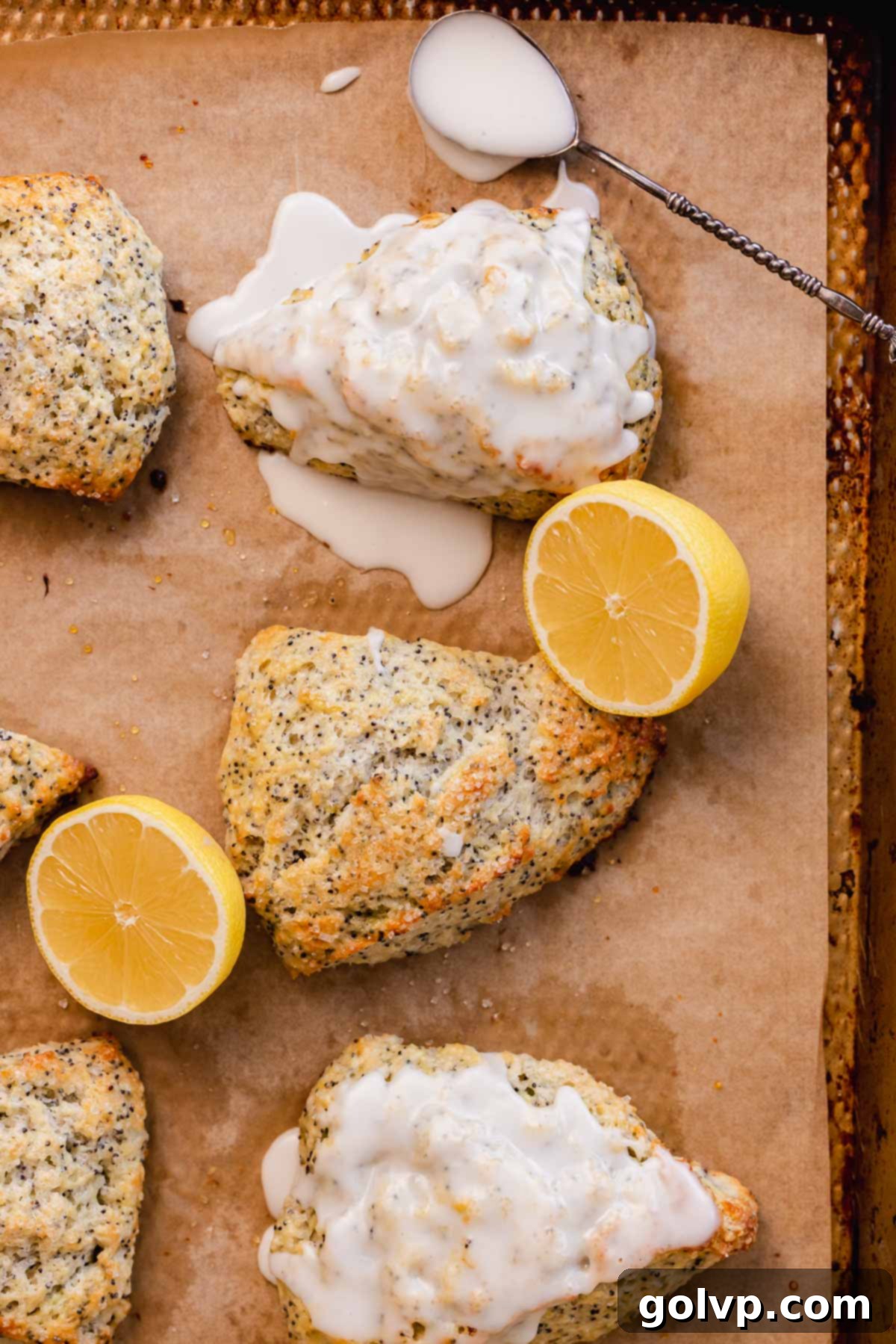 Baked and glazed lemon poppy seed scone on parchment paper with a bowl of lemon glaze nearby