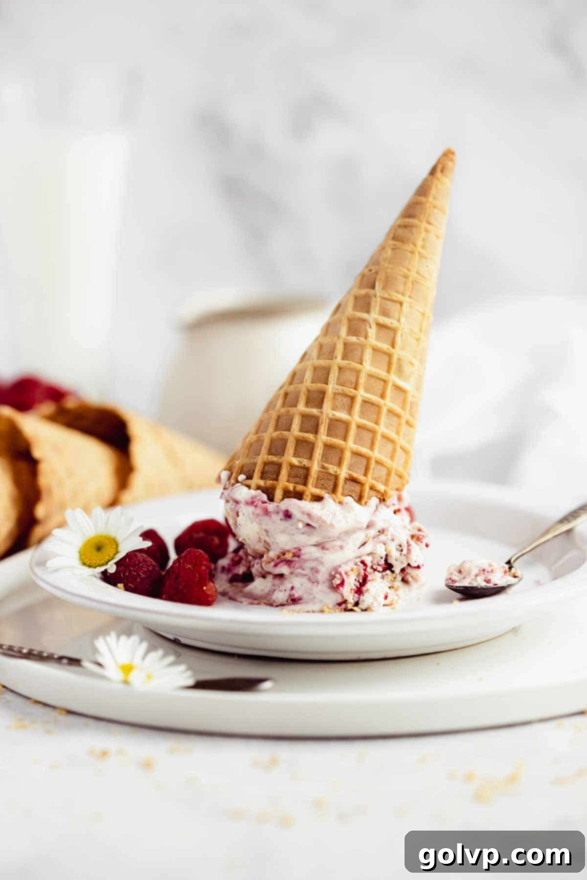 Upside-down waffle cones on plates with scoops of ice cream and fresh raspberries