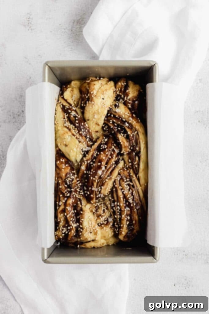Easy No-Knead Chocolate Tahini Babka 12 Braided and risen babka loaf in a pan, topped with sesame seeds and ready for baking