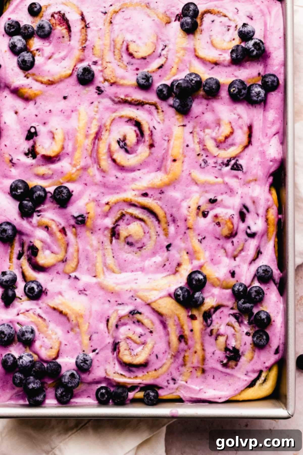 Finished blueberry cinnamon rolls with glossy blueberry cream cheese glaze and fresh blueberries as garnish