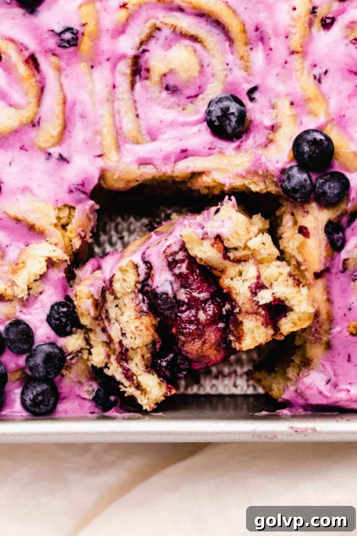 Half of a baked blueberry cinnamon roll showing its soft texture and generous blueberry filling in a baking tray