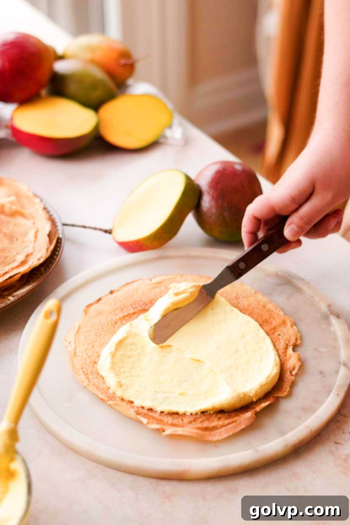 Decadent Mango Crepe Cake, Made Easy 14 Spreading a thin, even layer of mango filling onto a crepe with an offset spatula.