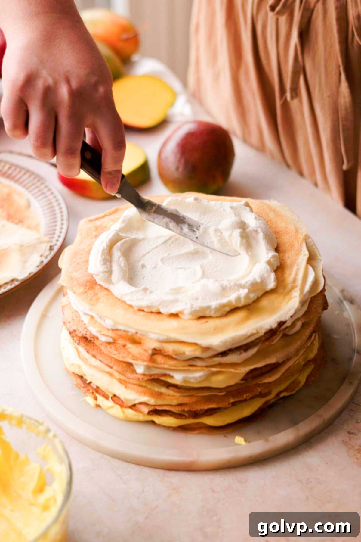 Decadent Mango Crepe Cake, Made Easy 16 Decorating the top of the layered crepe cake with swirls of white whipped cream.