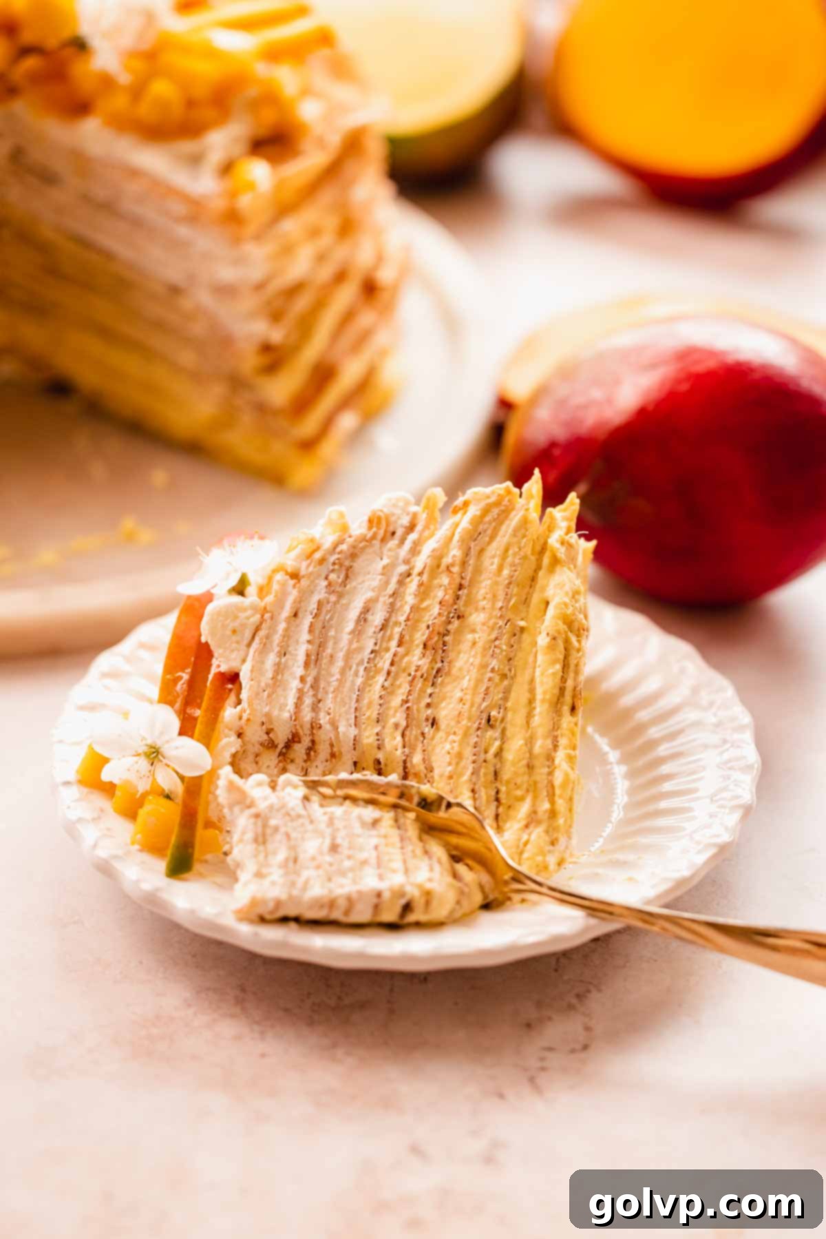 Decadent Mango Crepe Cake, Made Easy 20 A slice of mango crepe cake lying on its side, with a fork poised to take a bite.