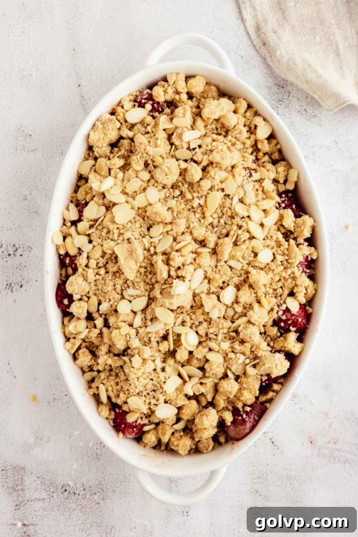 Crumble topping being sprinkled over strawberries in a baking dish.