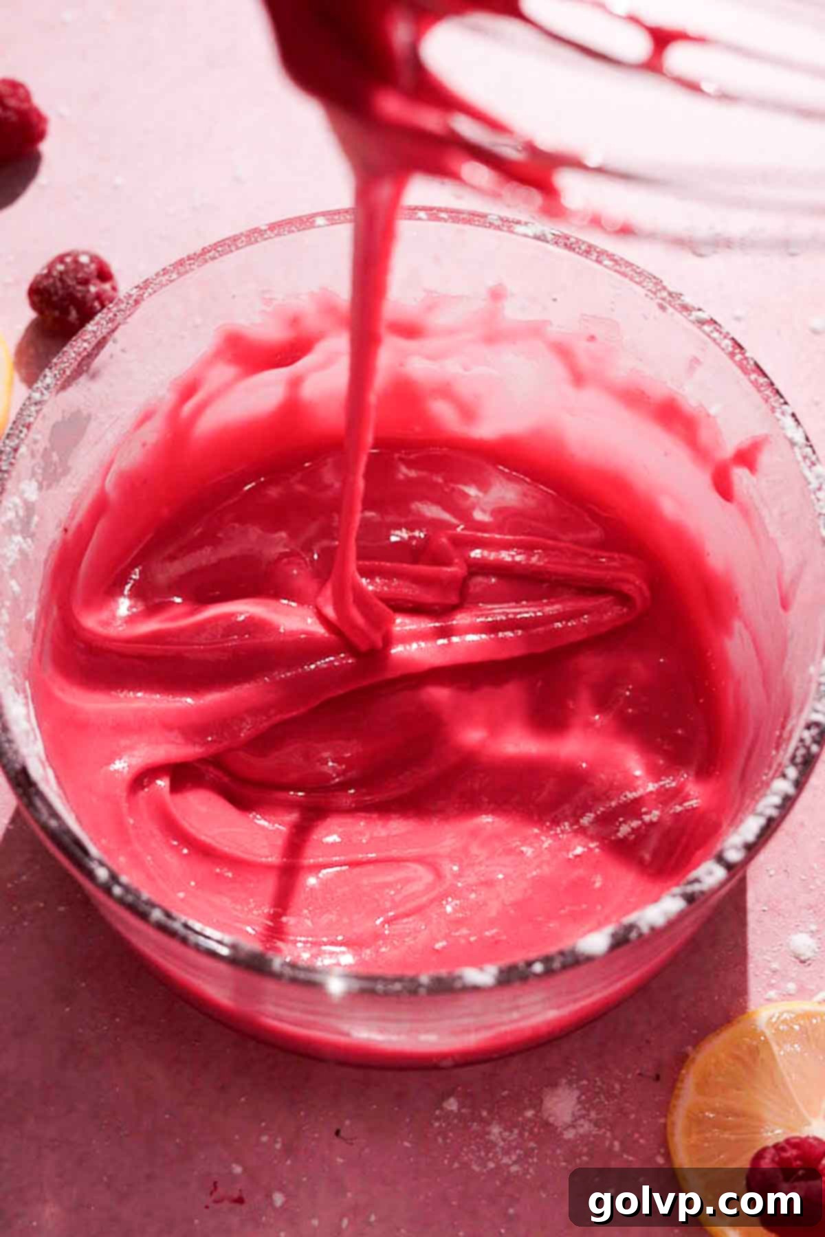 thick ribbon consistency of raspberry glaze icing falling off whisk