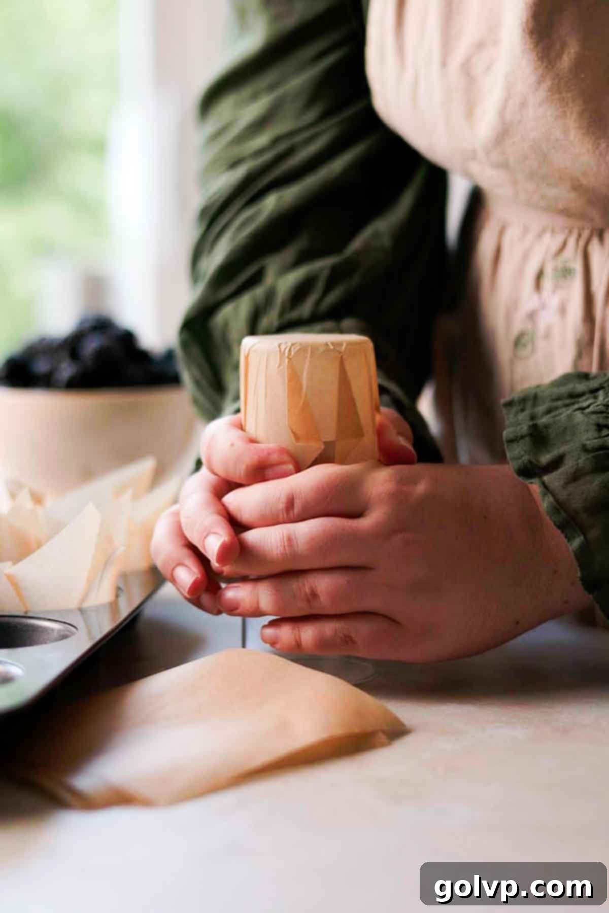 Pressing a square of parchment paper over an inverted glass to form a muffin liner.