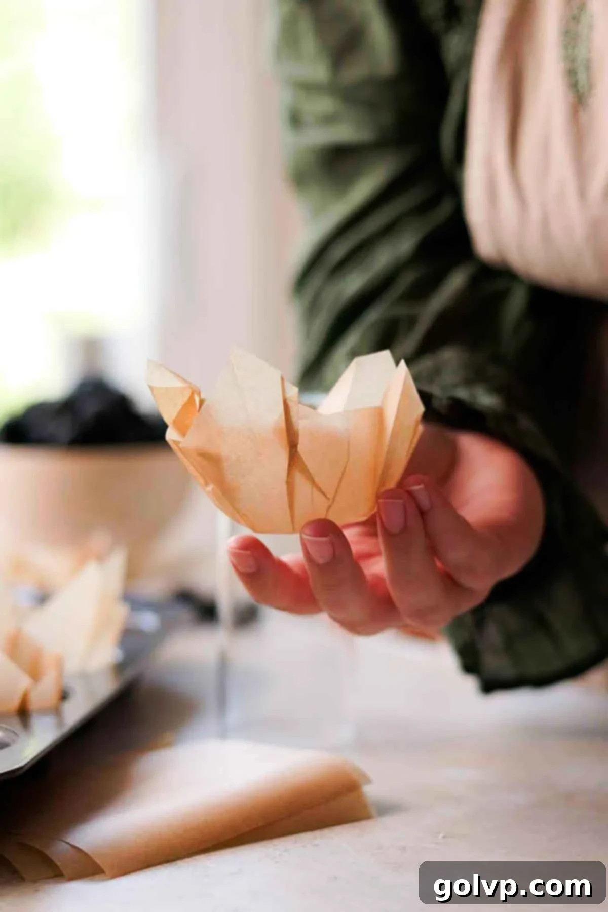 Holding a finished DIY parchment paper muffin liner in hand, ready for the muffin tin.